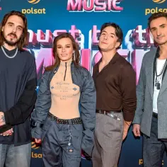 Czterech artystów na ściance z napisem "must be the music". Wokalistka w odważnej stylizacji z tatuażami na dekolcie.