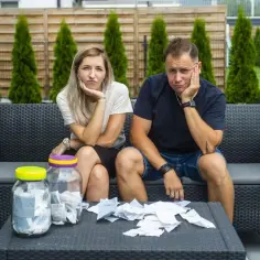 Zmartwieni uczestnicy programu "życie na kredycie" siedzą na kanapie, otoczeni rachunkami.