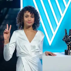 Młoda artystka w białej sukni z trofeum "The Voice Kids" w dłoni, symbolizującym zwycięstwo.