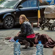 Kobieta w czarnej ramonesce klęczy obok zakrwawionej osoby na drodze. W tle czarny samochód i wózek dziecięcy. Czy to lipowo zmowa milczenia?