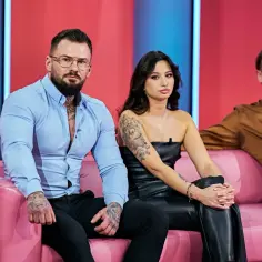 Uczestnicy "Love Never Lies Polska" siedzą na różowej kanapie. Mężczyzna w niebieskiej koszuli i kobieta w czarnym topie mają tatuaże.