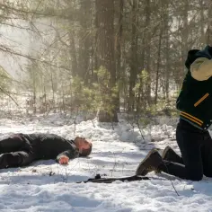 W lesie, na śniegu, leży nieprzytomny mężczyzna. Obok niego klęczy młody chłopak z podniesionymi rękami, jakby w obronie. Scena z Dexter: New Blood.